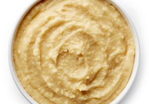 Bowl of homemade hummus isolated on white background from top view