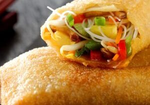 Crispy fried spring roll with filled with fresh vegetables and sprouts for delicious Chinese cuisine on a wooden table with chopsticks