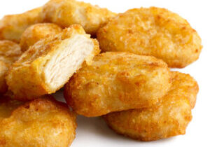 Pile of golden deep-fried battered chicken nuggets isolated on white. One cut with meat showing.